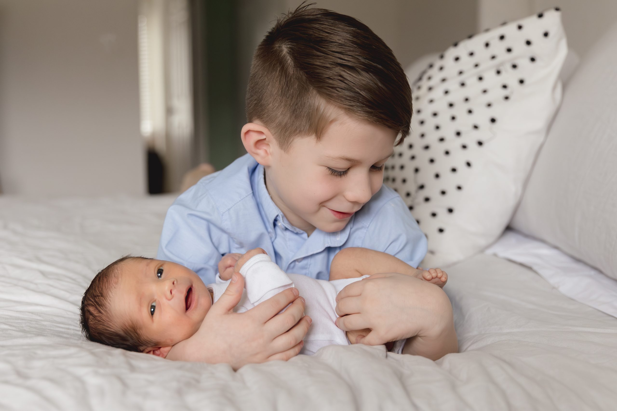 big brother holds newborn smiling little brother